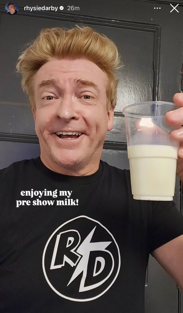 Screenshot from rhysiedarby’s IG story he is clean shaven and making a goofy little smiling face wearing his R⚡️D shirt and holding a cup half full of milk text on the image says enjoying my pre show milk and I said oh I bet