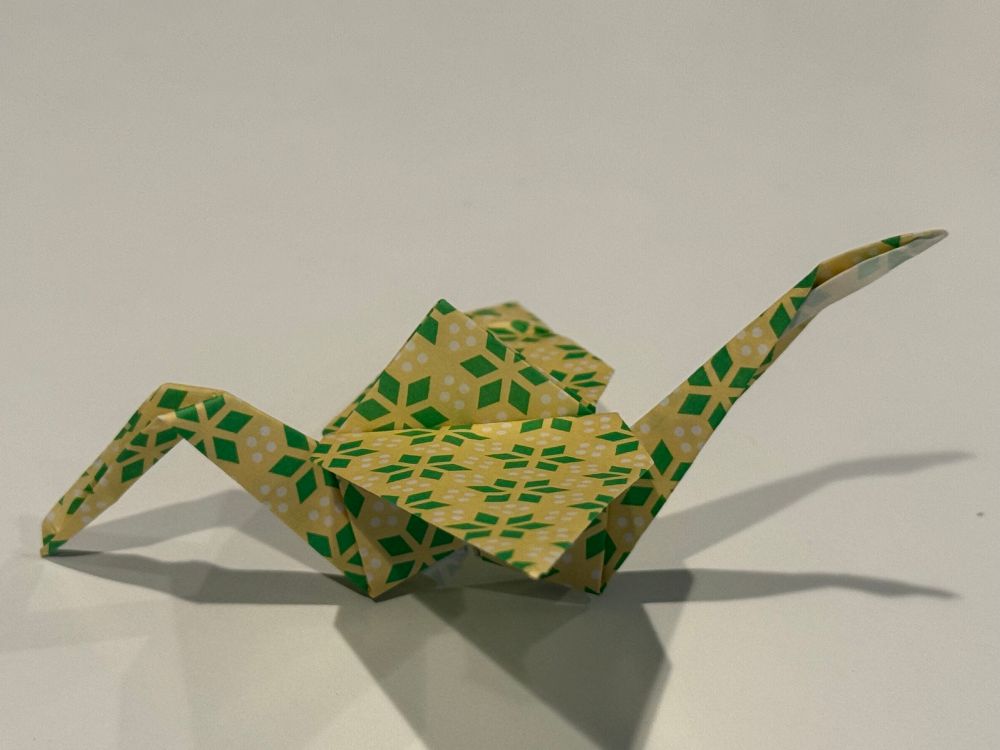 A folded paper crane with a pattern of green diamond flowers on a yellow background. 