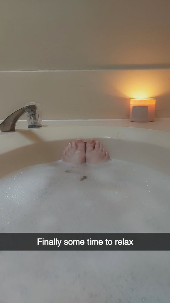 A photo of a bubble bath with woman's toes peeking out of the bubbles and a candle lit on the edge of the tub. Caption says "Finally some time to relax"