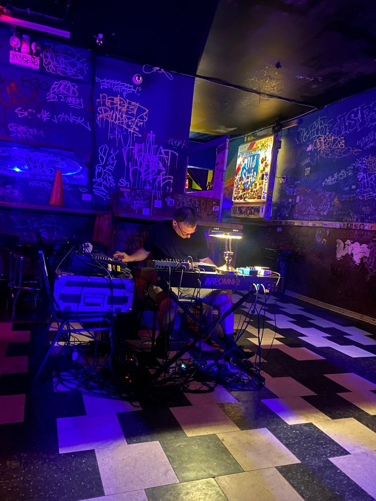 Guy sitting at a table with synths and a desk lamp