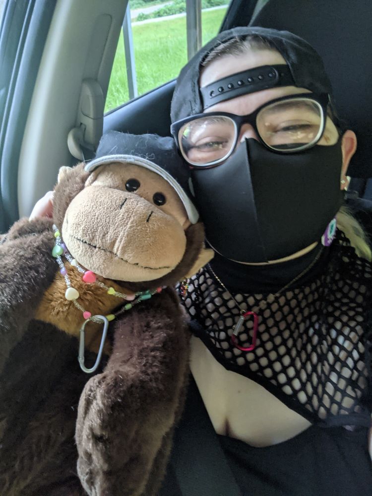 Me holding a monkey backpack dressed similarly to myself. We are both wearing a hat, a necklace with a carabiner hanging off it, and earrings. 