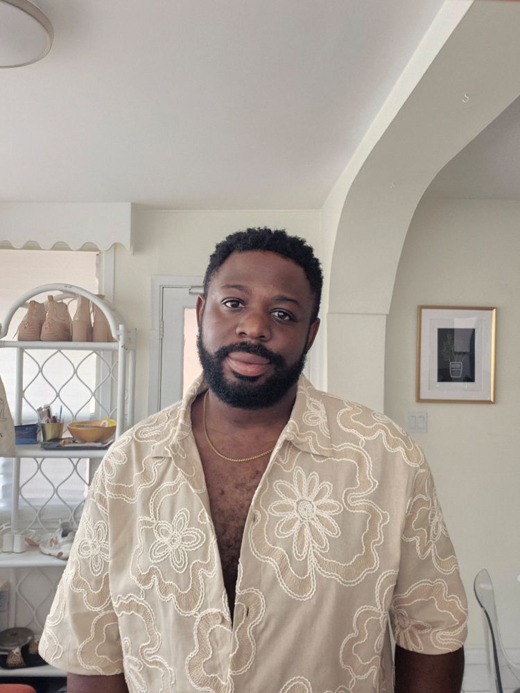 A black man in a floral, buttercream, short sleeve button up.