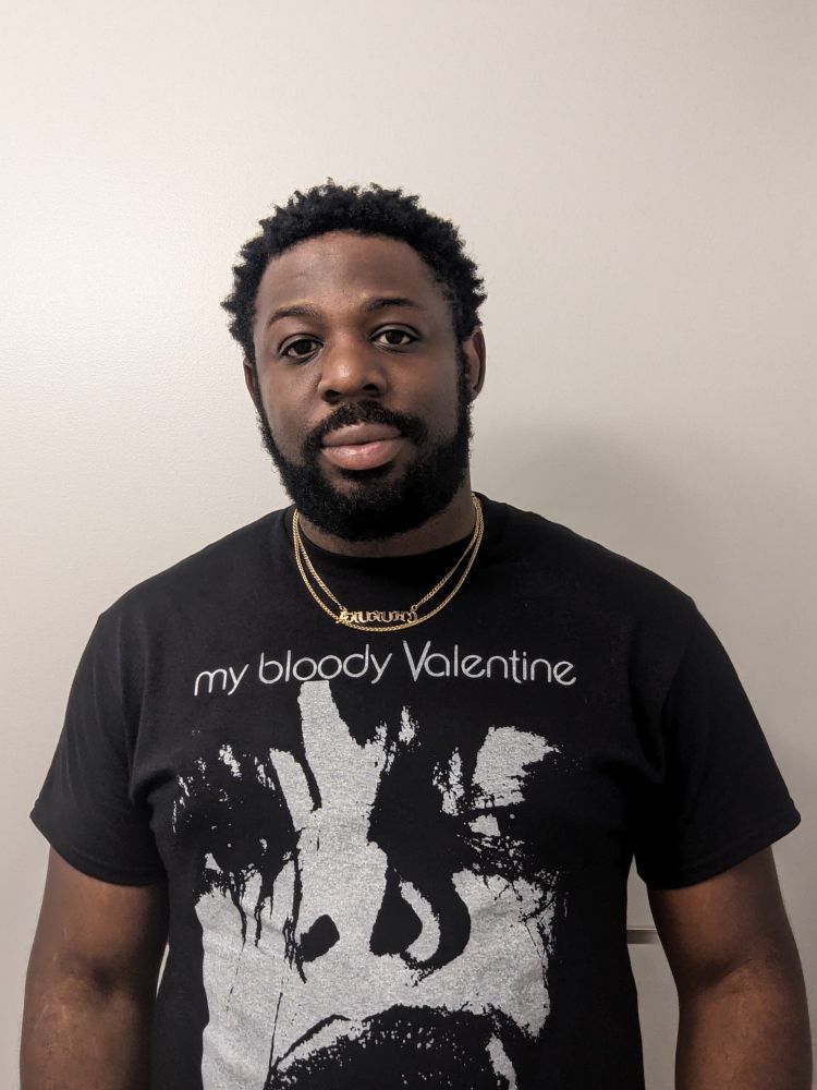 A picture of myself in a black shirt posted against a white a wall.