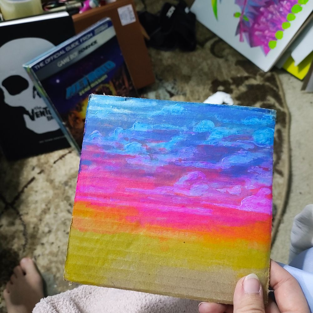 piece of square brown cardboard painted in blue, pink and yellow paint to look like a sky at sunset.

very vibrant dark hues
from top to bottom- blue, pink and yellow. the blue area has the most fluffy clouds, the disappear through pink and yellow.