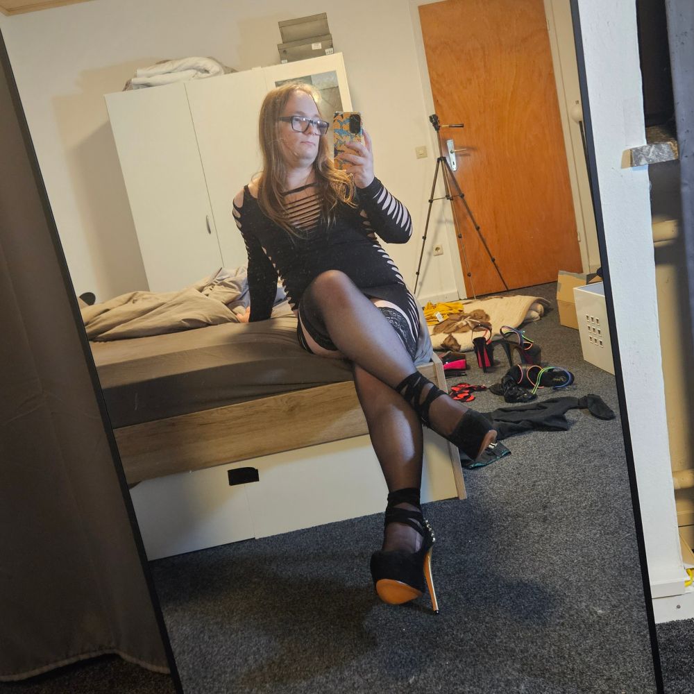 Me sitting on the edge of my bed, legs crossed. Wearing a black dress, nylon stockings and heels