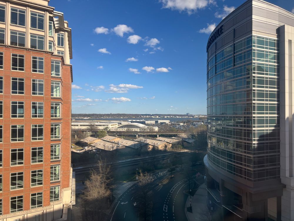 A view between 2 tall buildings of Reagan National Airport and the Potomac. The sky is blue with small scattered white clouds. 