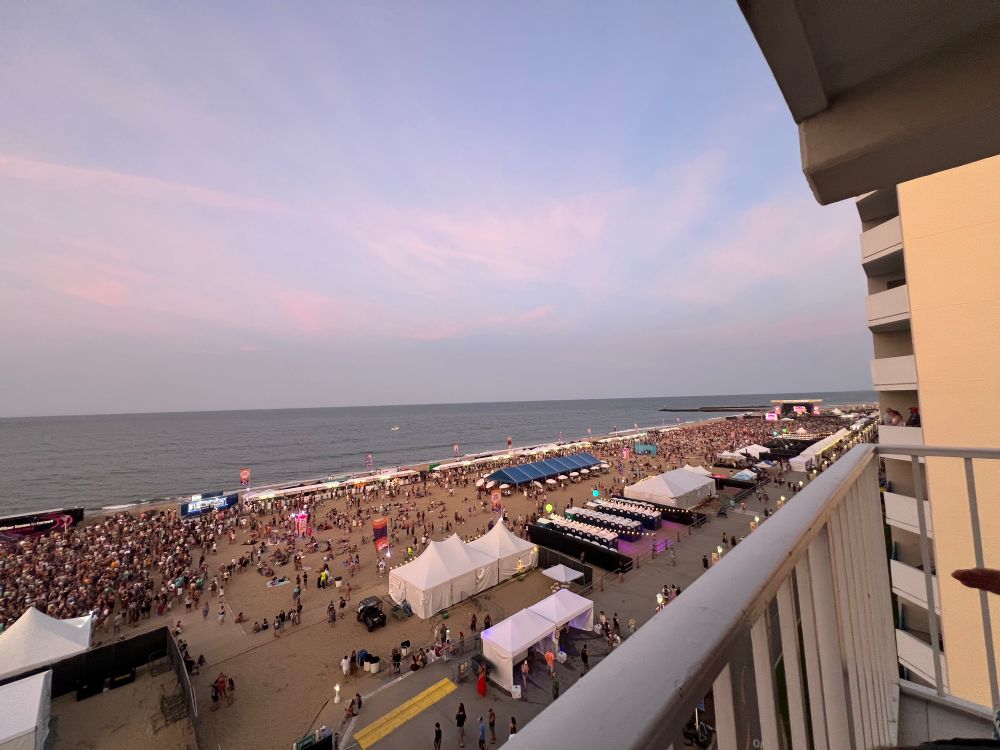 A music festival at a beach covered in event tents and people. The time of day is sunset. 