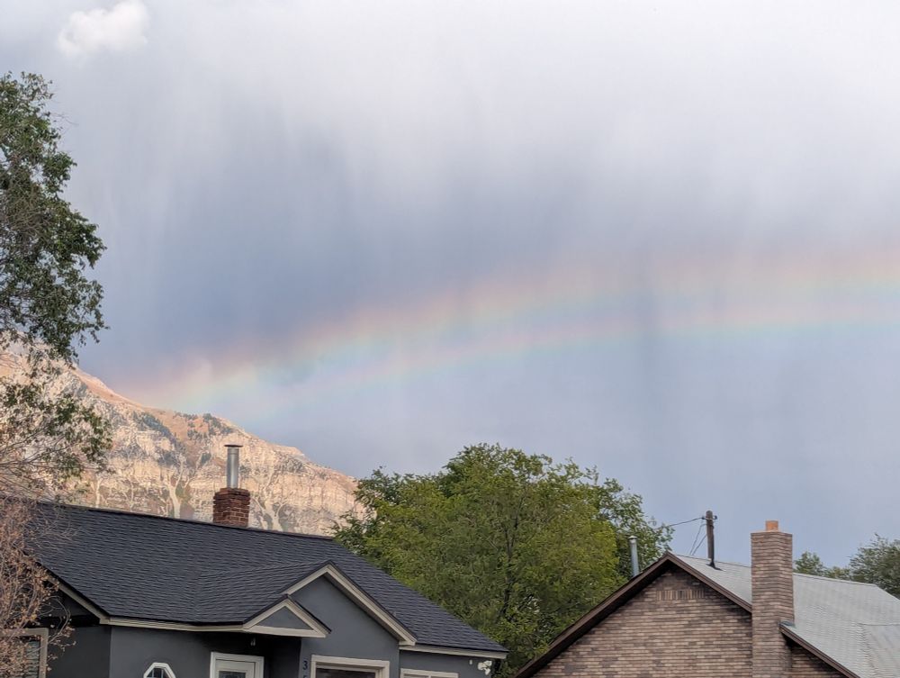 Closer view of left end of double rainbow in a distant cloudy/rainy gray sky. 