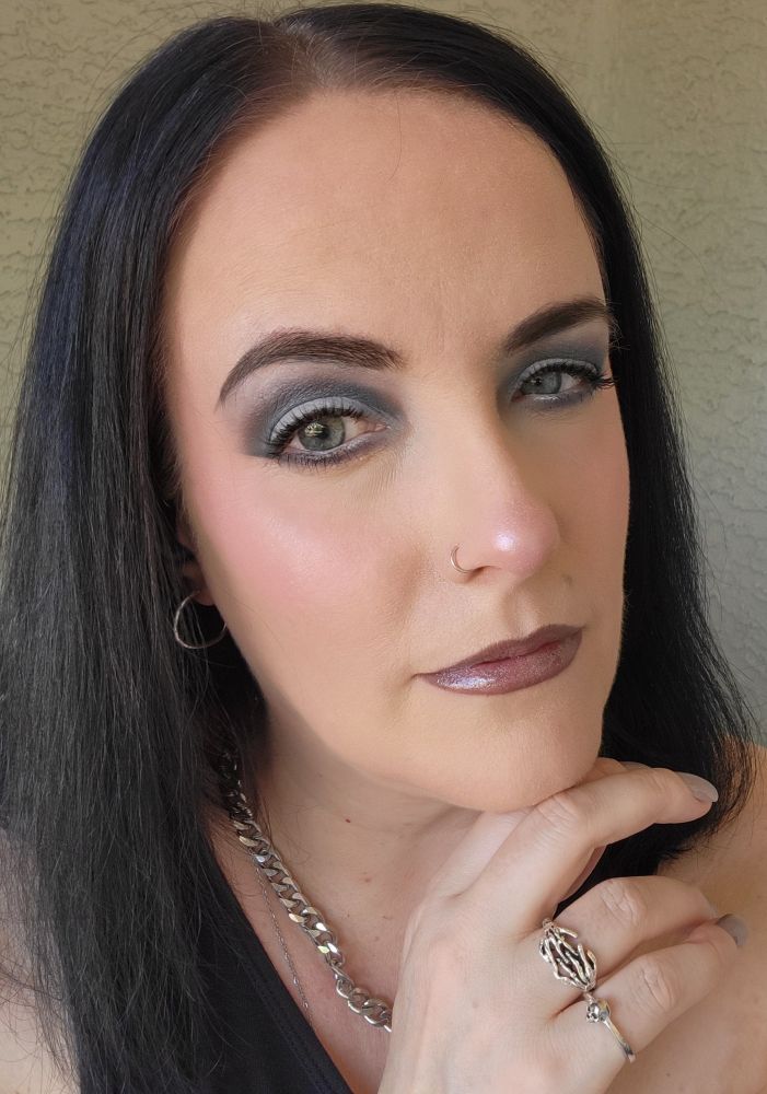 (Me) with medium, straight black hair posing with my hand near my chin, showcasing silver rings and a chunky chain necklace. The makeup look features bold, smoky blue-gray eyeshadow, defined brows, and glossy metallic mauve lipstick. Also visible is a small hoop nose ring and a sleeveless black top, with a neutral textured wall in the background.
.
.
.
Eyes: @themobbeauty x @jessicahazemua Trad Goth Collection
Additional details - @themobbeauty Volumizing Mascara, @iliabeauty Limitless Lash Mascara, @nyxcosmetics Jumbo Eye Pencil in Milk
Lips : @themobbeauty M159 liner and @jessicahazemua Peptide Drench Cushion Lip Gloss in shade Dark Star 
 
Face: @milkmakeup hydro grip primer, @pacificabeauty Hydrodew Slime Barrier Care Gel, @aboutfacebeauty Shadow Fix Eye Primer
@hauslabs foundation 040, 01 Fair Neutral concealer, Moonstone Bio Radiant Gel Powder highlighter
@westmanatelier Biscuit bronzer stick
@themobbeauty x @courtneyquarantine - cream clay blush M150
@makeupbymario soft blur setting powder in 2 Neutral Light