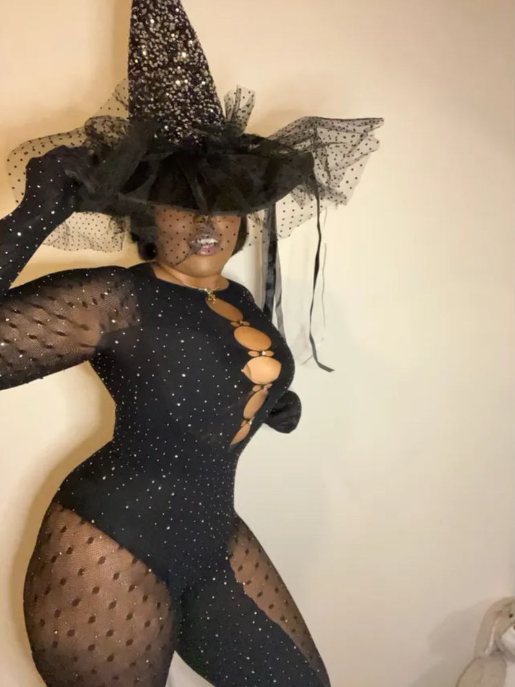 A Black woman in a black sparkly jumpsuit and a witch’s hat