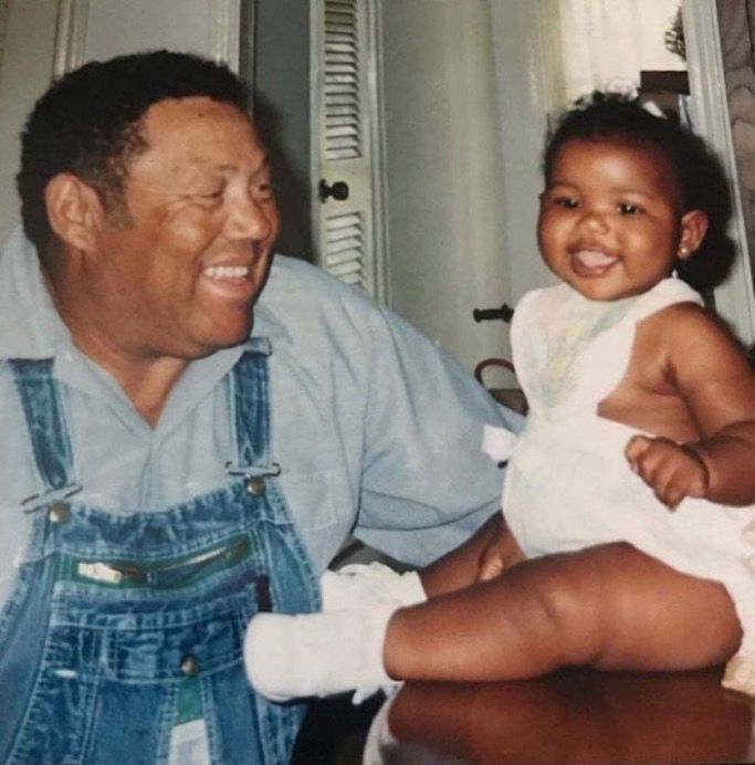 A man in a blue shirt and overalls next to a baby on a table in a white onesie