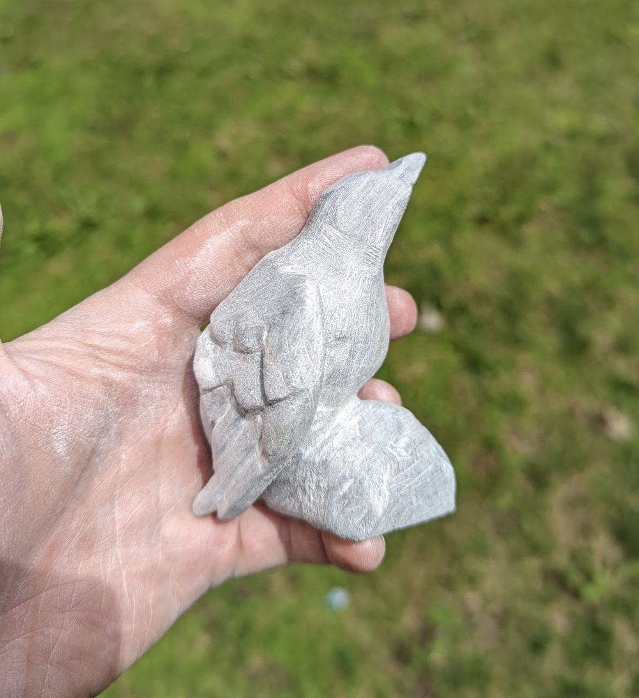 hand holding a rough cut sculpture of a perched bird. The stone is grey and roughly carved