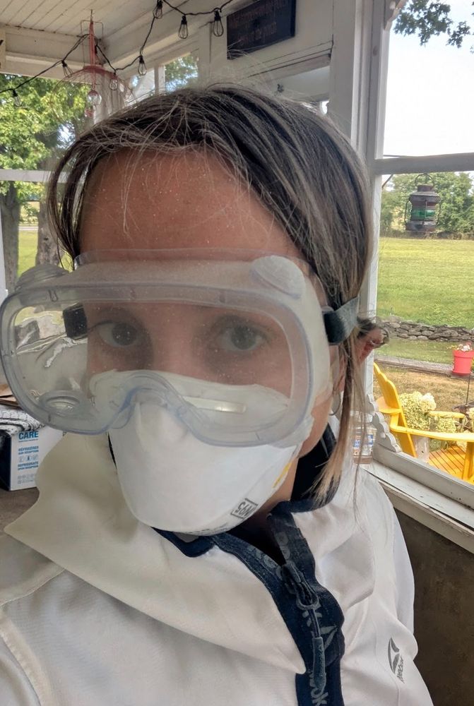 Photo of someone wearing protective gear — white top, n95 mask, goggles. Their hair is coated in white dust. 