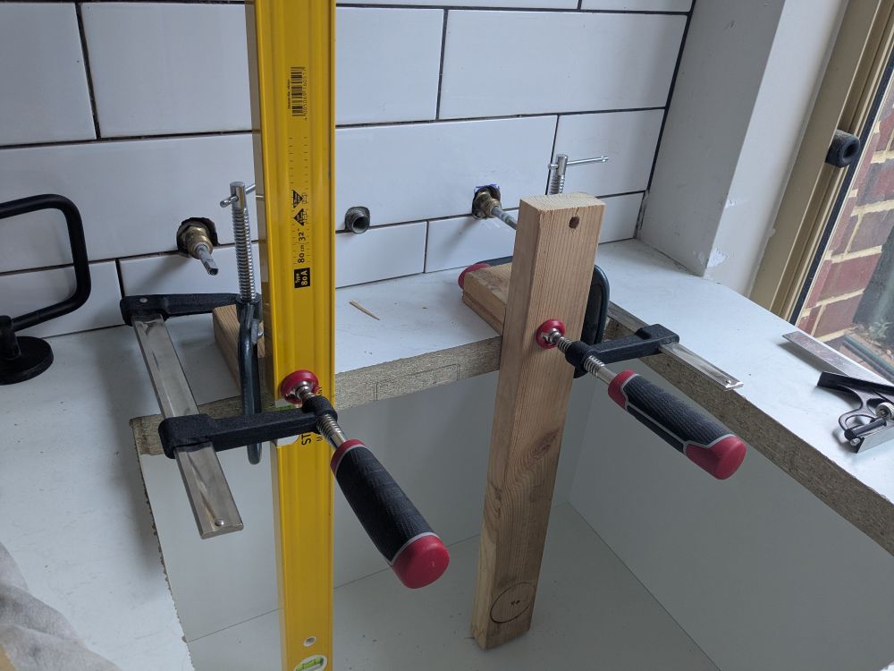 Rig made of four clamps, scrap wood, and a spiral level, for making a small routed groove in a laundry sink cutout.