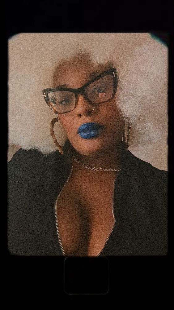 Pretty Black woman with a white afro, cat eye glasses, gold hoops, and blue lipstick