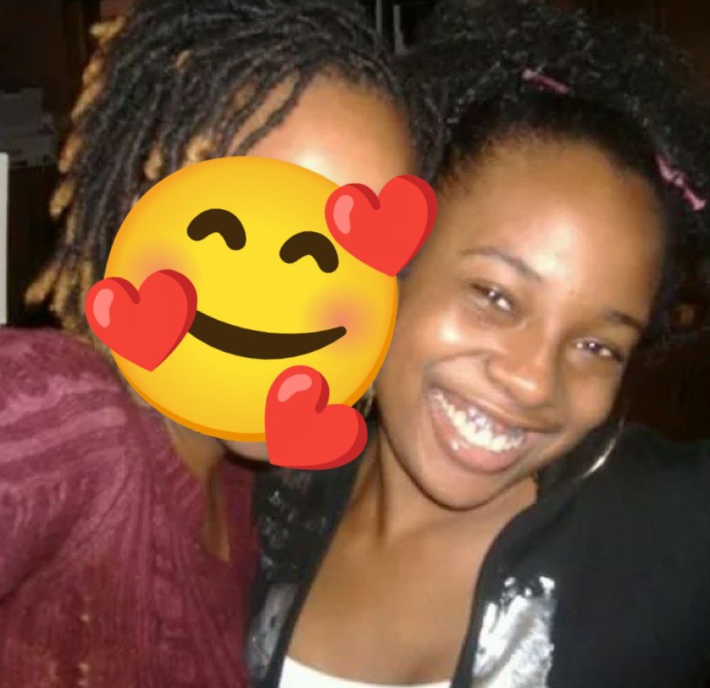 Pretty Black girl with a curly puff and a Black, white, and silver top smiling into the camera