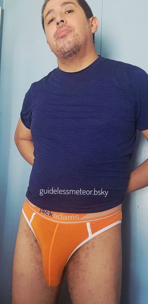 A man in a blue shirt and orange briefs, waiting for a good sub to get on his knees. 