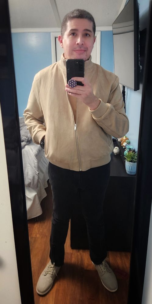 A man stands shows off his outfit which has beige and black colors.