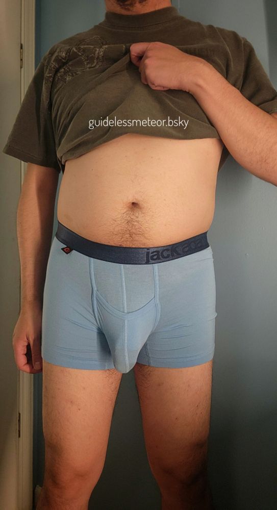 A man stands with a full belly and a bulge in his blue boxer briefs. He's waiting for you to get on your knees and worship. That's your purpose.