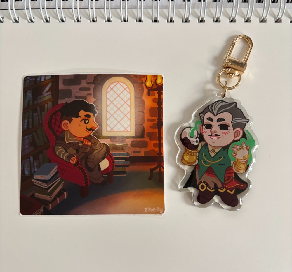 Photo of a sticker of Dorian from Dragon Age Inquisition and an acrylic charm of Emmrich from Dragon Age The Veilguard