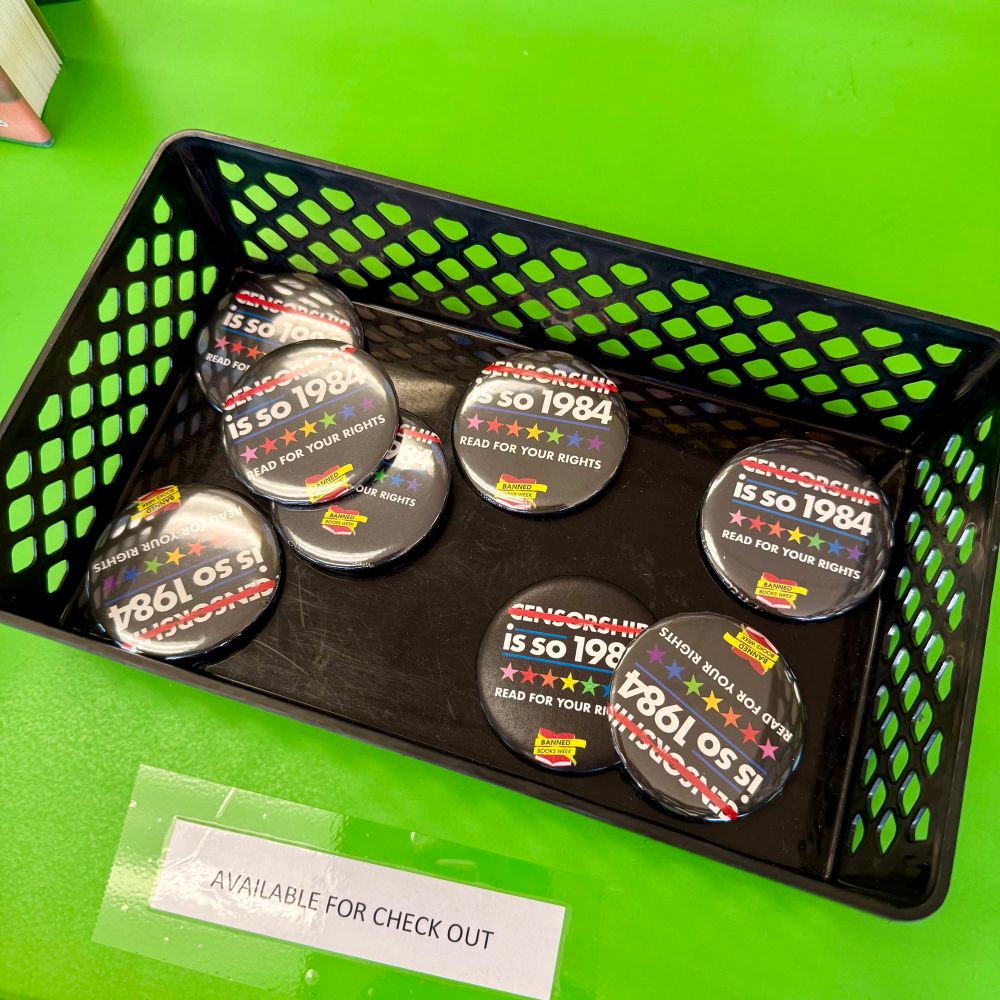 A photo of pins that reads “CENSORSHIP (strikes through) is so 1984” in a basket seen at a local public library.
