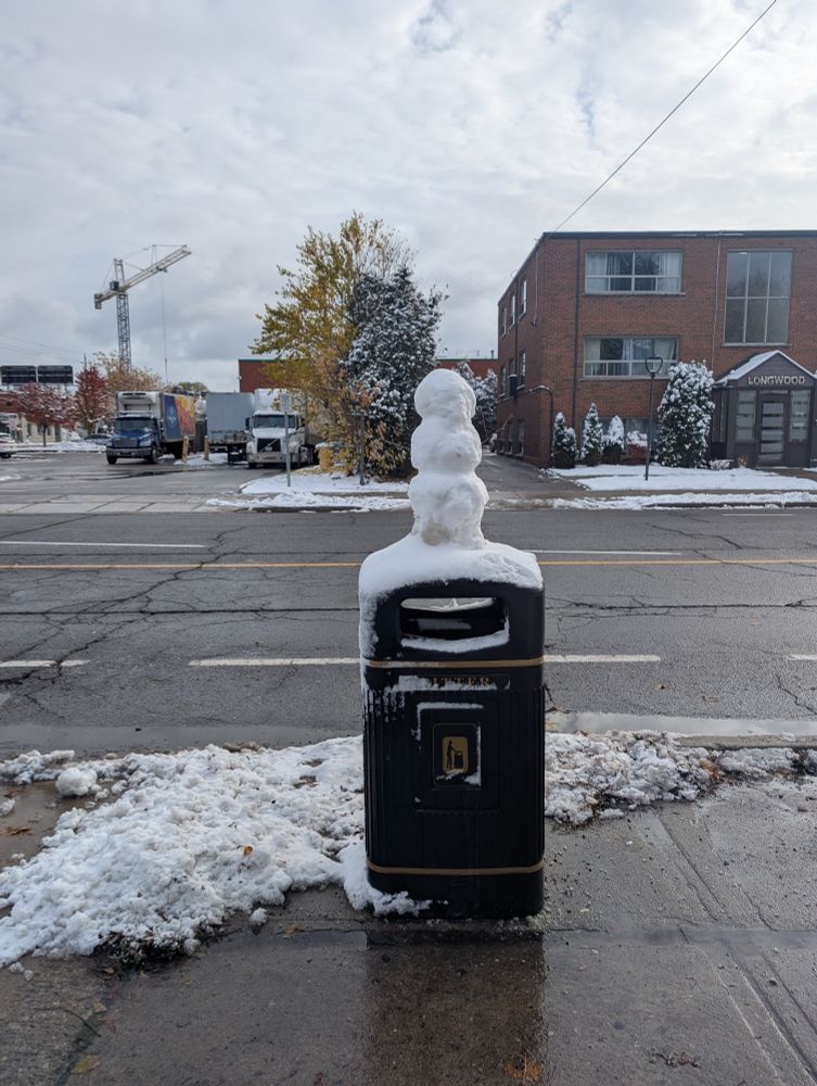 A very small snowman built on top of a garbage can