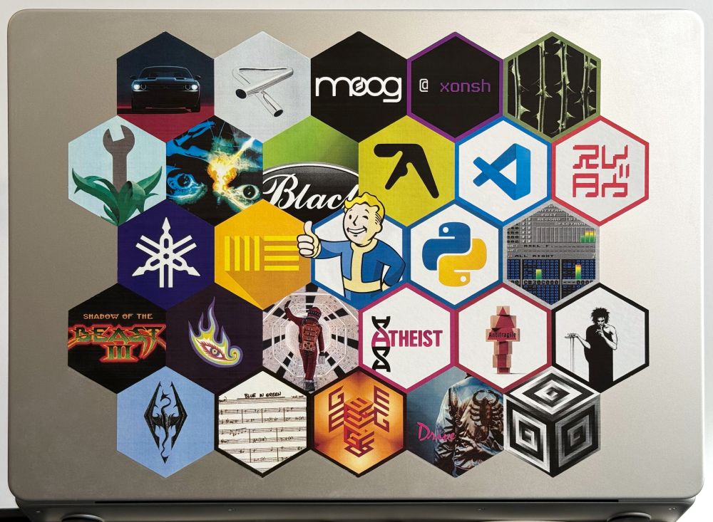 A picture of a laptop with a large sticker on it that emulates a 6 x 5 grid of hexagonal stickers. Depicted are things I like. Dodge Challenger, Tubular Bells, Moog Music, Xonsh, October Rust, Zen and the Art of Motorcycle Maintenance, Flashback, Black (the auto-formatter), Aphex Twin, Visual Studio Code, Yamaha Revstar hanko, Yamaha Corporation triple tuning fork logo, Ableton Live, Fallout, Python (the programming language), ProTracker 2, Shadow of the Beast 3, Tool (the band), Dave Bowman walking through Discovery in “2001: A Space Odyssey”, Atheism, Antifragile, Sandman, Elder Scrolls, Miles Davis’ “Blue in Green” sheet music from the bootleg 5th edition of the “Real Book”, Godel Escher Bach, Drive (the movie), and Supercollider (the music synthesis server).