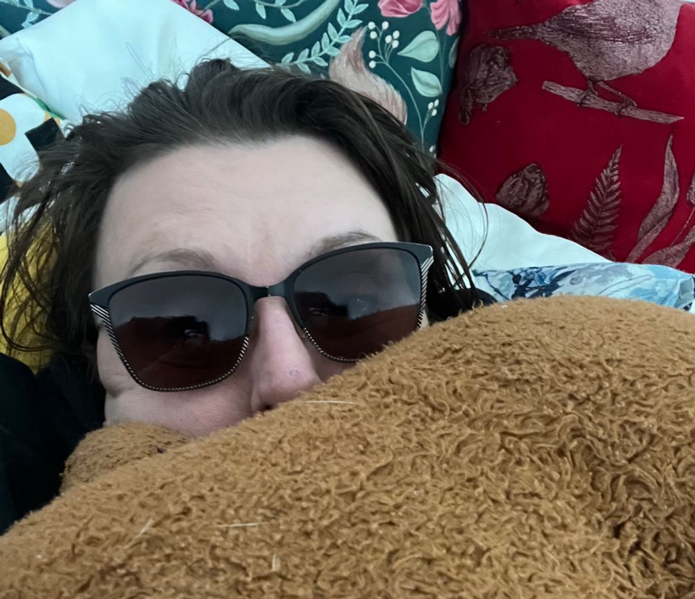 A photo of me in bed with a teddy bear covering my face 