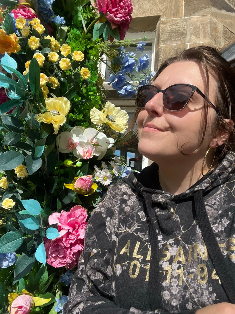 A photo of me next to a garland of plastic flowers 