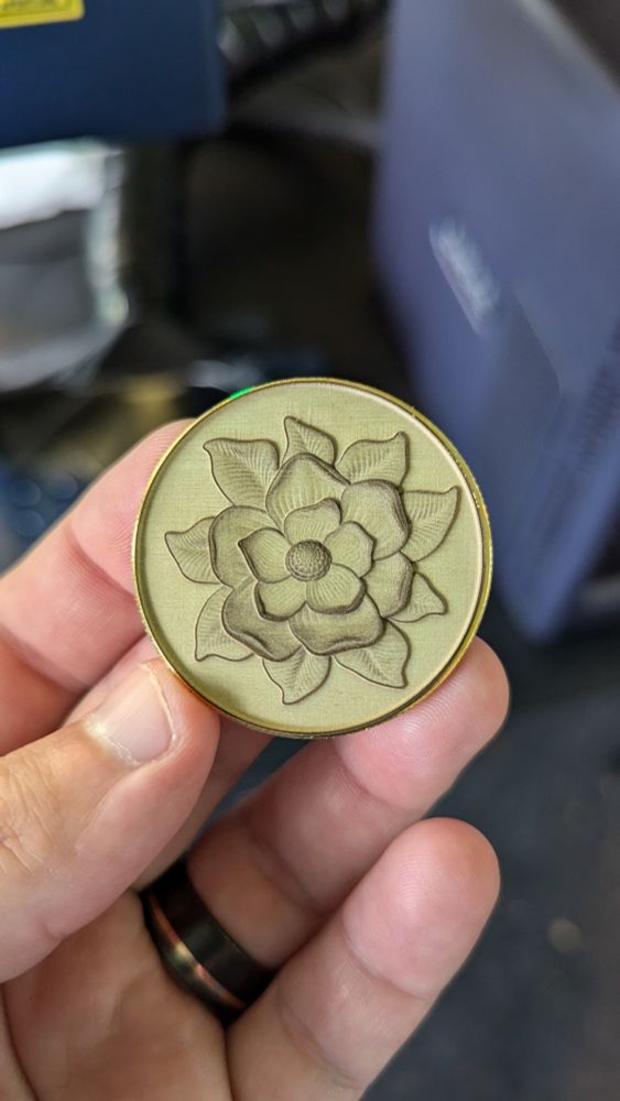 A brass coin with a flower engraved into it, held in a person's hand. 