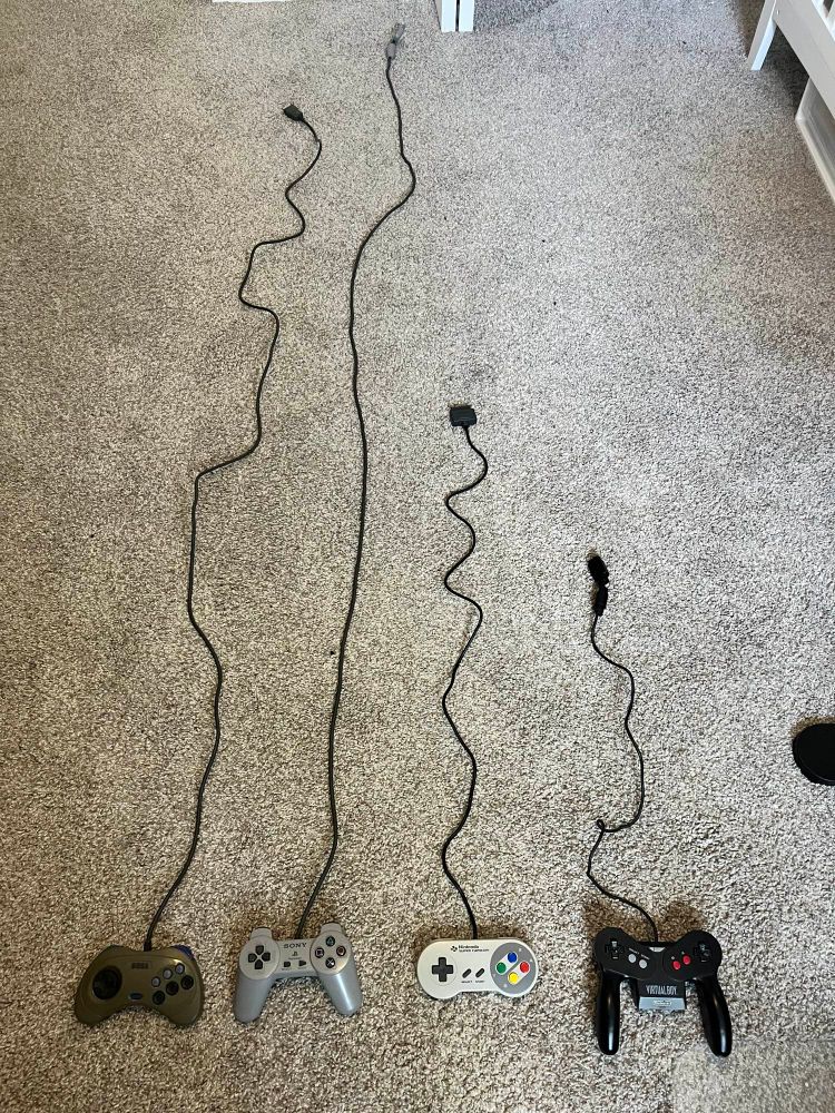 Four controllers lined up on the floor, showing cord length. JPN Saturn, PS1 Digital, Super Famicom, Virtual Boy