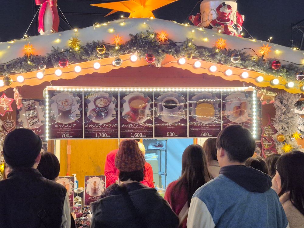 Bude mit warmen Getränken; u. a. heiße Schokolade, Orange, Kaffee (wahlweise mit oder ohne einer Tasse in Form eines Weihnachtsstiefels) und kleine Creme Puffs