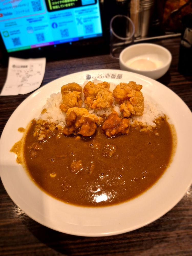 Japanisches Curry mit frittierten Hähnchenstücken, Käse untergemengt und Reis auf einem Teller sowie einem weichen Ei in einer kleinen Schale daneben.