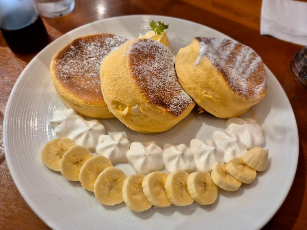 Japanische Pancakes, davor eine geschnittene Banane schön drapiert mit kleinen Sahneklecksen