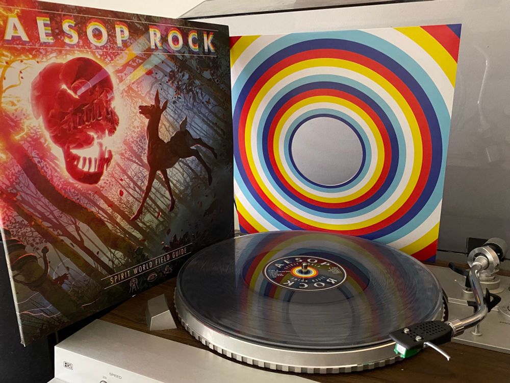 Aesop Rock’s Spirit World Field Guide album cover and insert behind translucent vinyl record on record player.