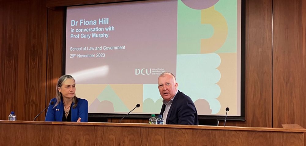 Image of Fiona Hill and Gary Murphy in conversation, wood panel walls & PowerPoint screen in DCU branding to the rear