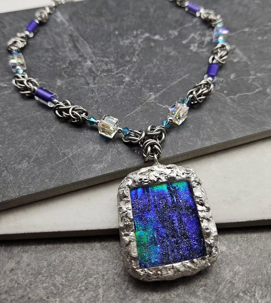 A dichroic glass pendant set in silver with a chainmail and bead chain. 