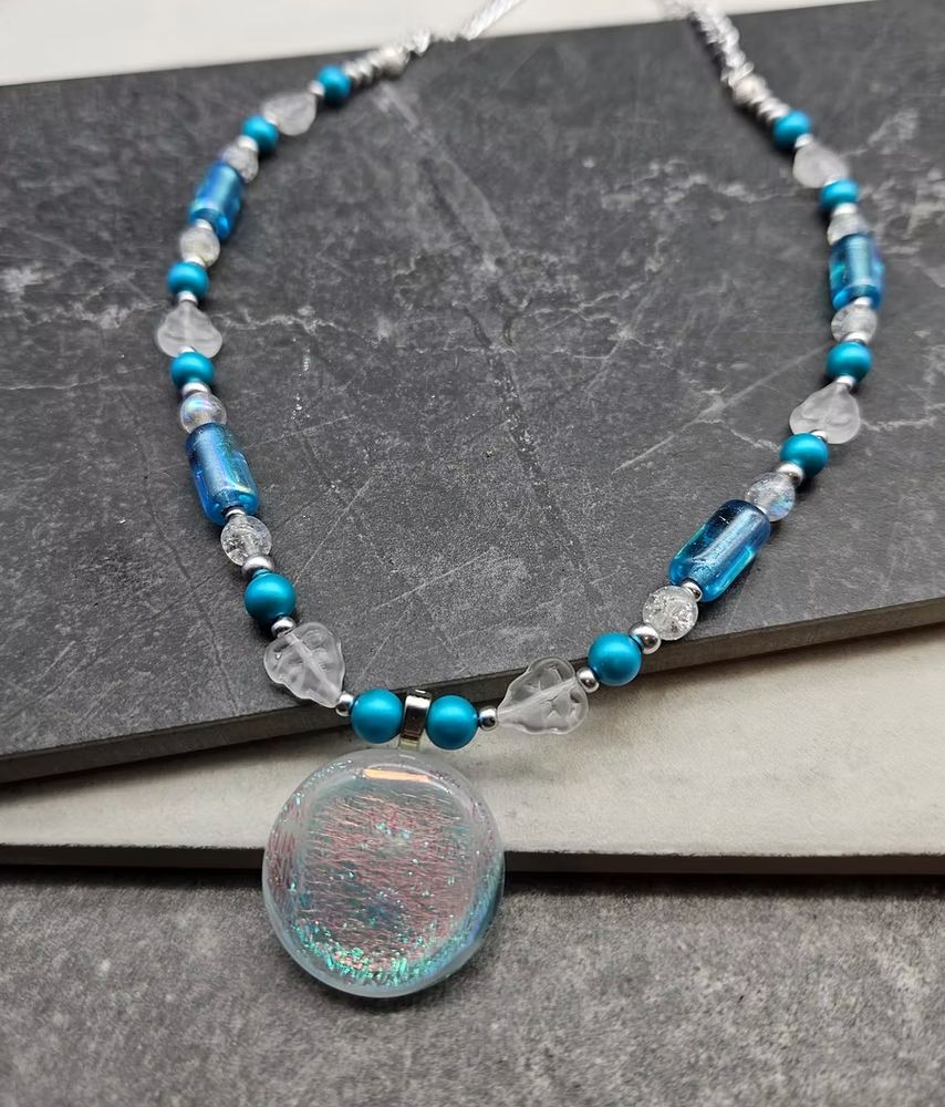 A clear class and teal bead necklace with a teal metallic glass pendant. 