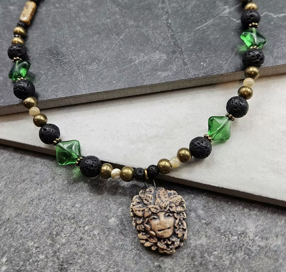 A green black and gold bead necklace with a forest spirit focal. 