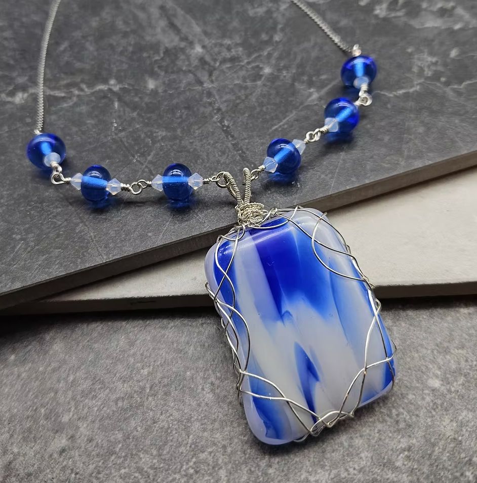 A wire wrapped white and blue glass pendant with a blue glass partial rosary chain 