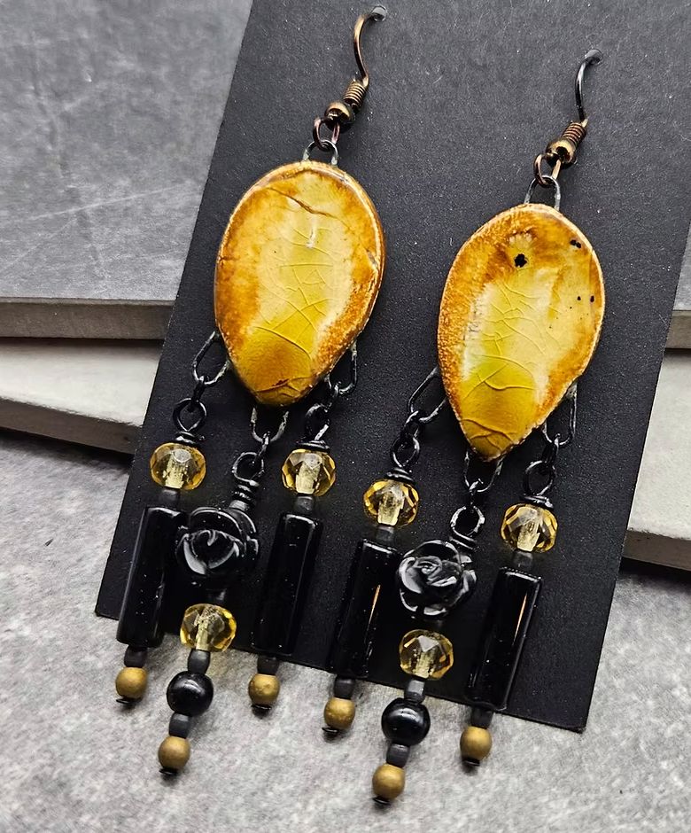 A pair of gold and black chandelier earrings with gold ceramic petals at the center and gold crystal and black flowers and beads suspended. 