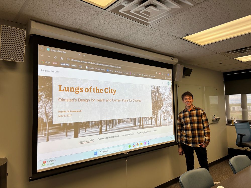 Schoenhardt, wearing a plaid flannel shirt and smiling, standing by the home page for his StoryMaps site reading, Lungs of the City.