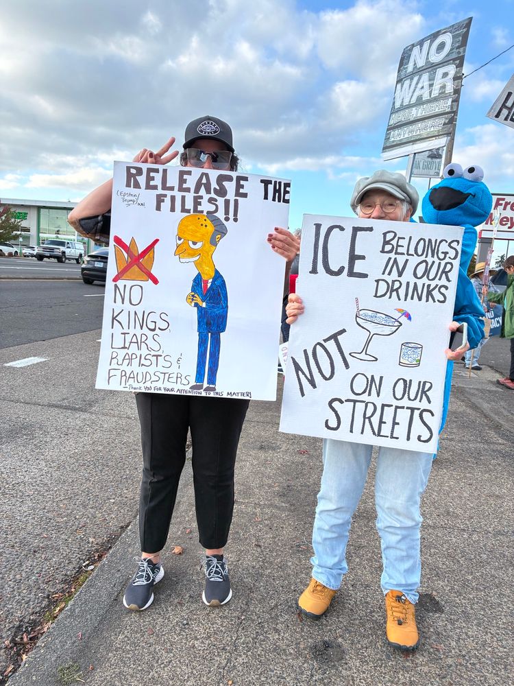 Citizens with protest signs !  On the left, sign reads, “Release the files!! (Epstein/Trump, duh!).. Bo Kings, liars, rapists & fraudsters—Thank YOU FOR YOUR ATTENTION TO THIS MATTER!”
  On the right, sign reads,”ICE belongs in our drinks, NOT on our streets.” Sign is embellished with drawings of two cocktails, one in a margarita-type glass, but with an umbrella.. the other is a standard tumbler. 