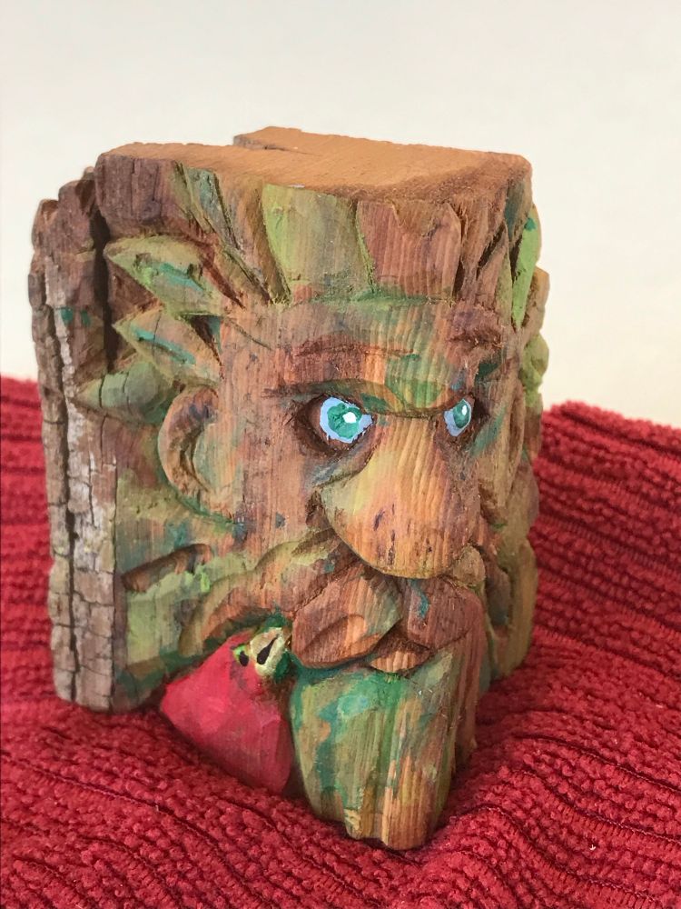 A green man, carved from cottonwood bark.. he’s about 3” tall. His face is framed by simple foliage; & his companion, a small red bird, is at his lower left.