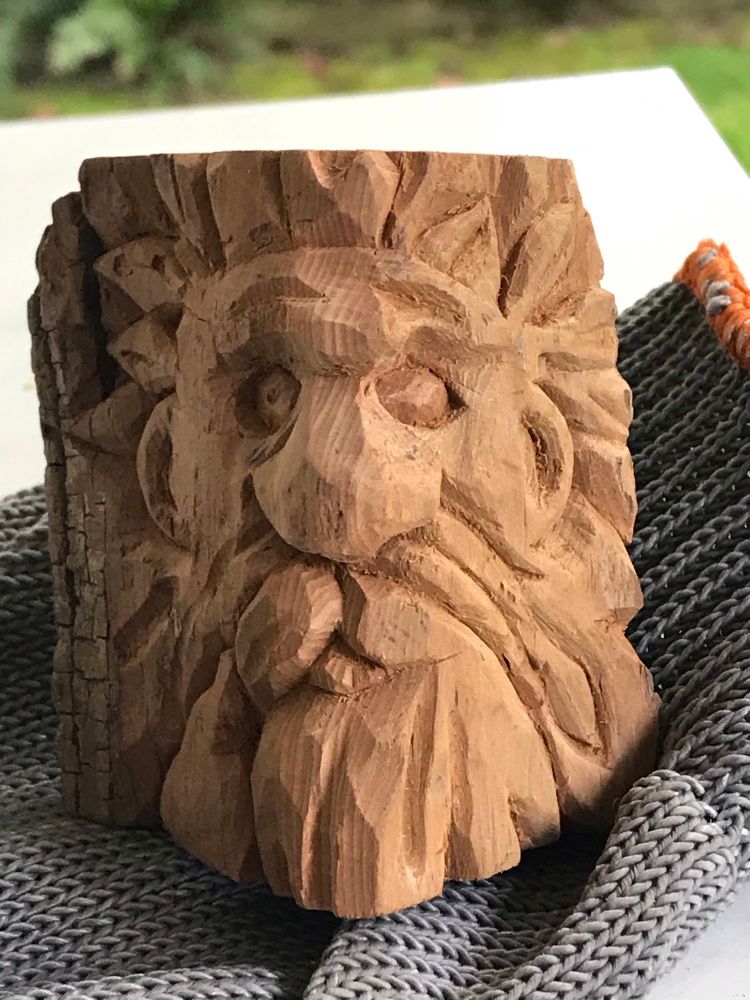 Wood spirit hewn from cottonwood bark. Piece is aprx 3” tall. Face is framed by leaves; small companion bird carved into lower left. Piece is unfinished- needs some color & maybe.. oil? 