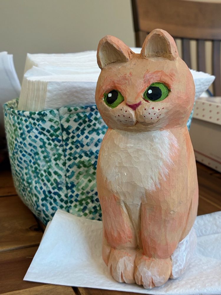 Cat, carved from basswood- aprx 4” tall. Acrylic paint, cream, buff-orange & white; & casting some green side-eye.