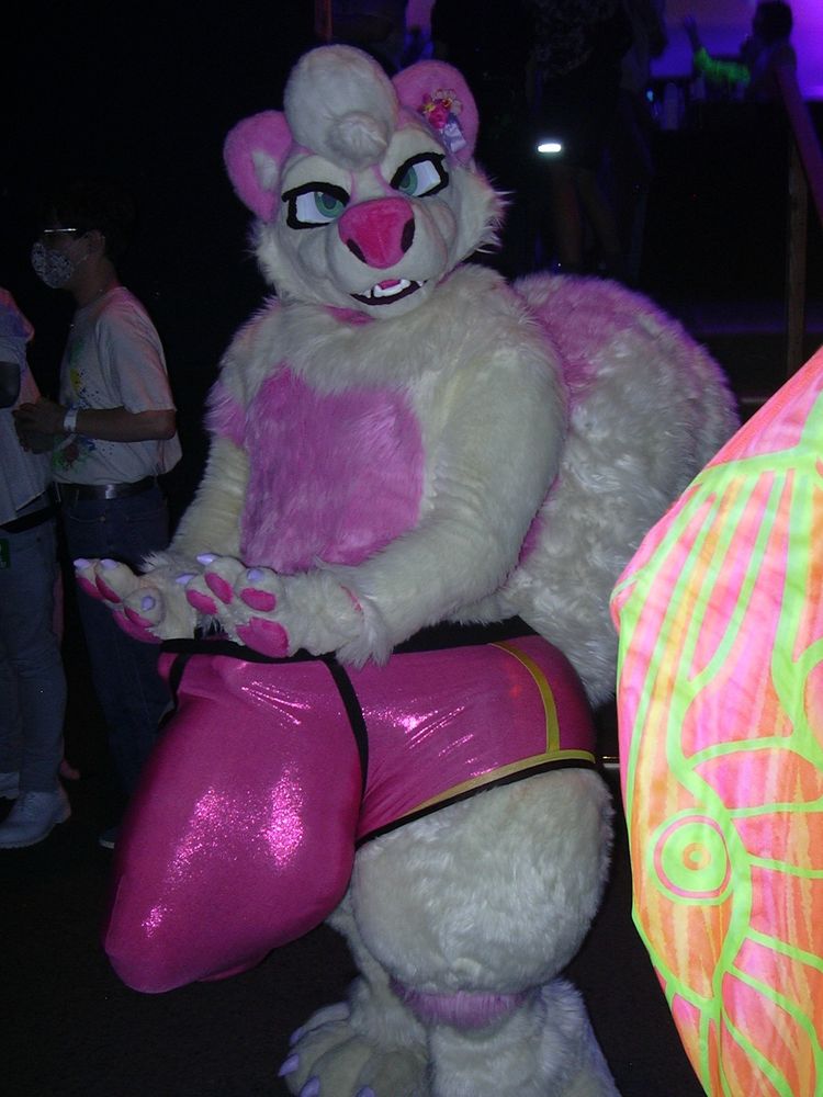 A digicam flash photo of Nargle the pink skunk in full fursuit. They are wearing a pair of oversized glittery pink underwear to contain their monstrous hyper bulge. They tug at their waistband with their thumbs.