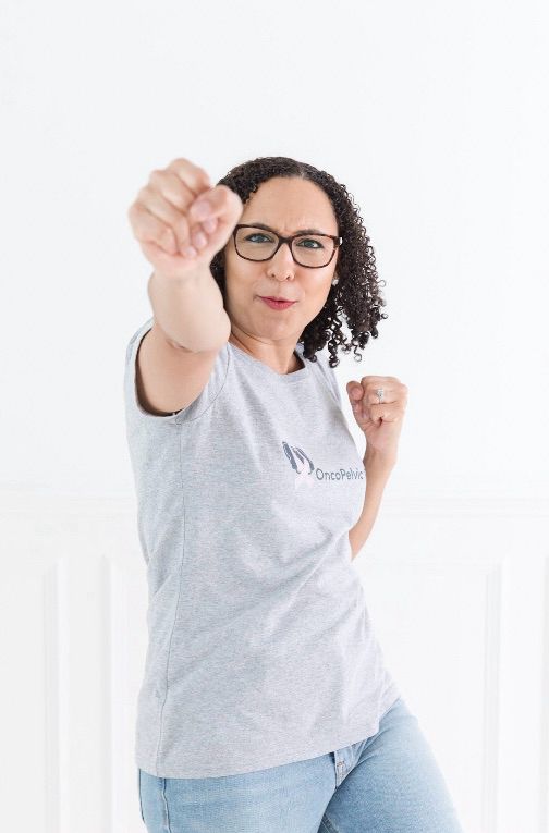 Alex wearing a grey OncoPelvic PT shirt and punching toward the camera 