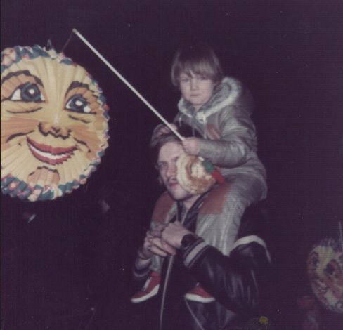 Space Wizard at 5 years old after the horrendous adventure of giving themselves a hair cut and a mom who had to fix it, sitting on the shoulders of their dad. They are carrying a lantern with a big moon face on it for the "Saint Martin's walk" back in 1984.