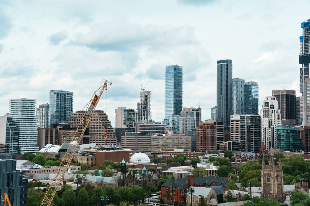 A photo of the Toronto skyline from the top of one of the University of Toronto buildings, showing the skyscrapers downtown and some of the greenery at UofT. There's a crane pointing up in the left side of the photo.